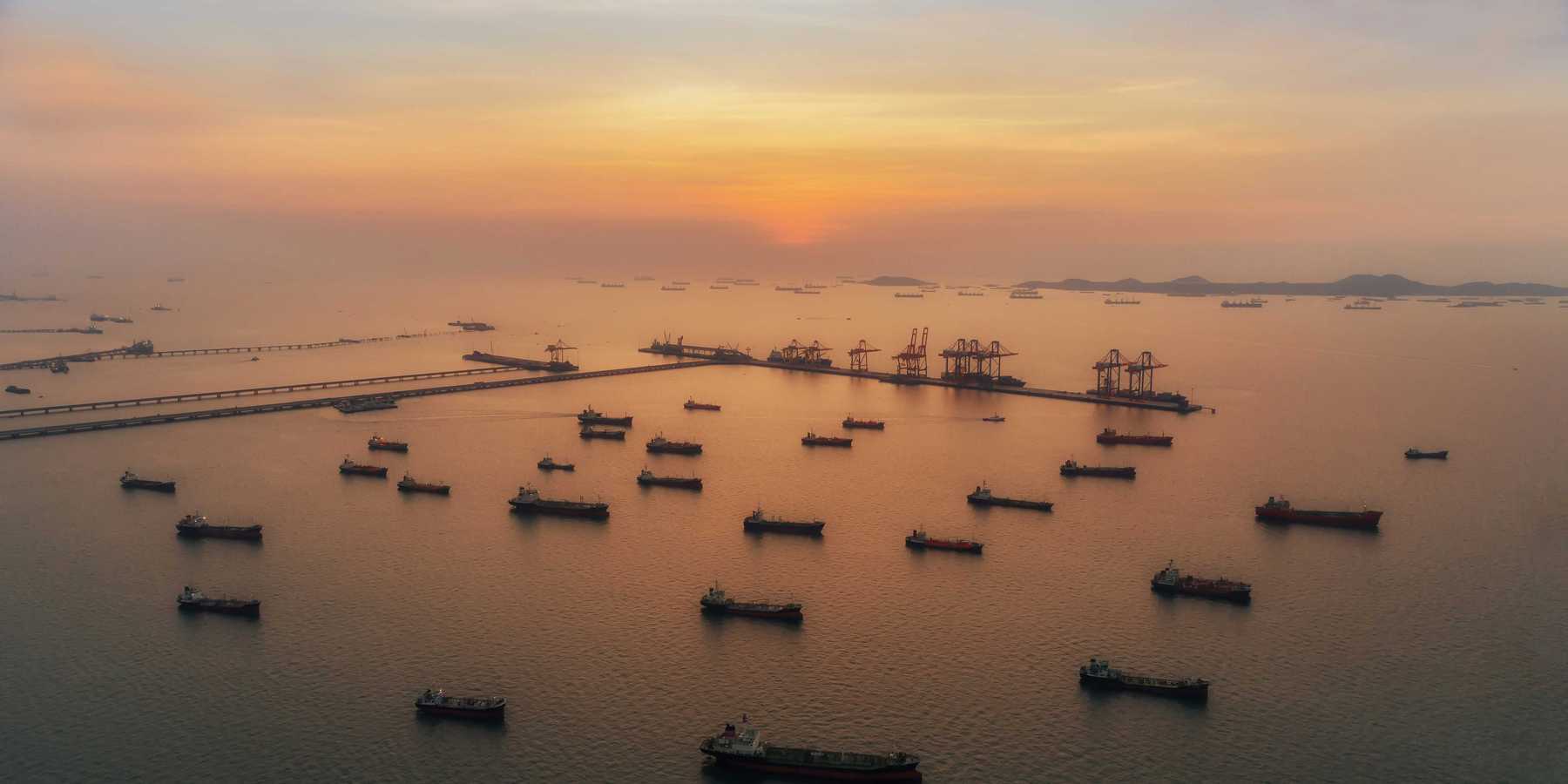 Oil tankers scattered across sea near port at sunset.