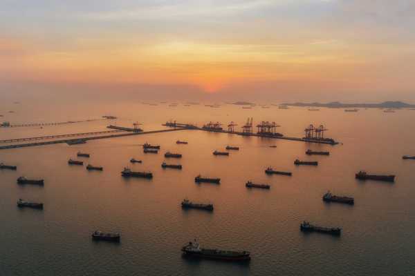 Oil tankers scattered across sea near port at sunset.