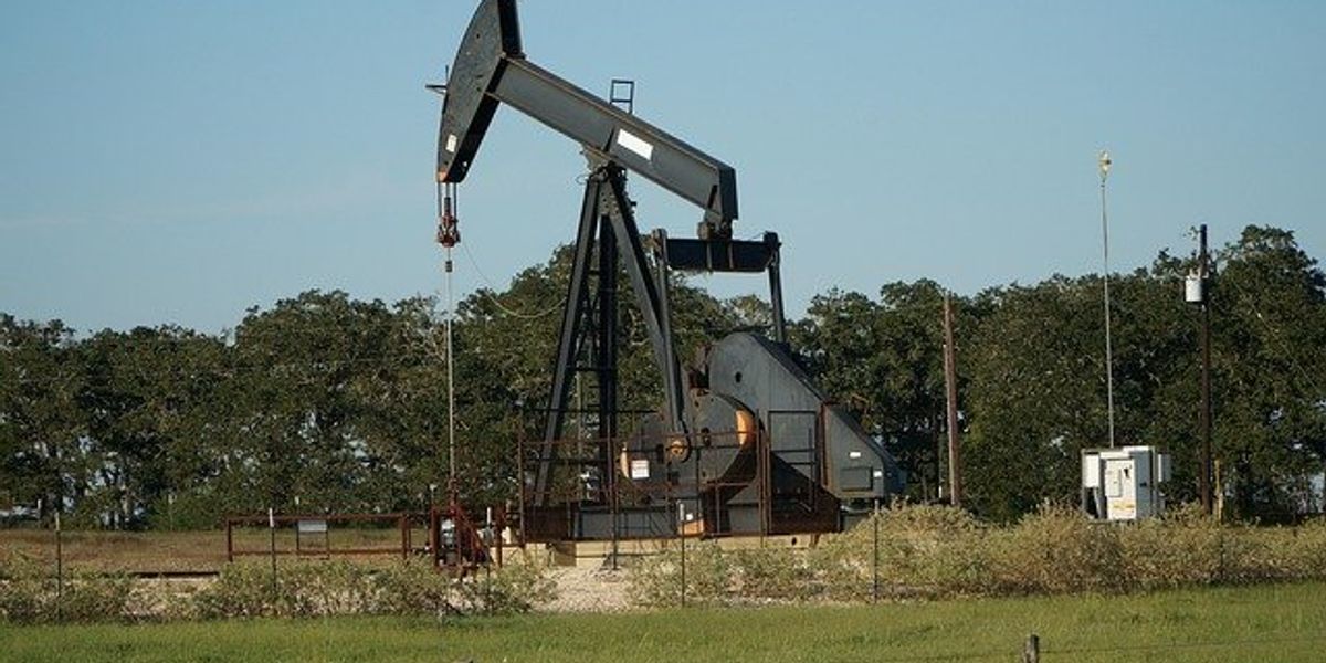 Oil well in the middle of a grassy field with trees in background.