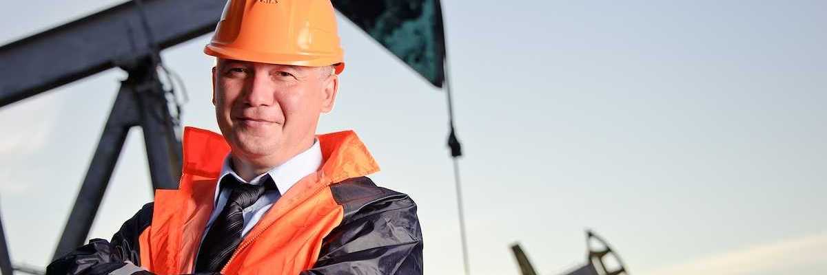 Oil worker in orange uniform and helmet on of background the pump jack and sunset sky.