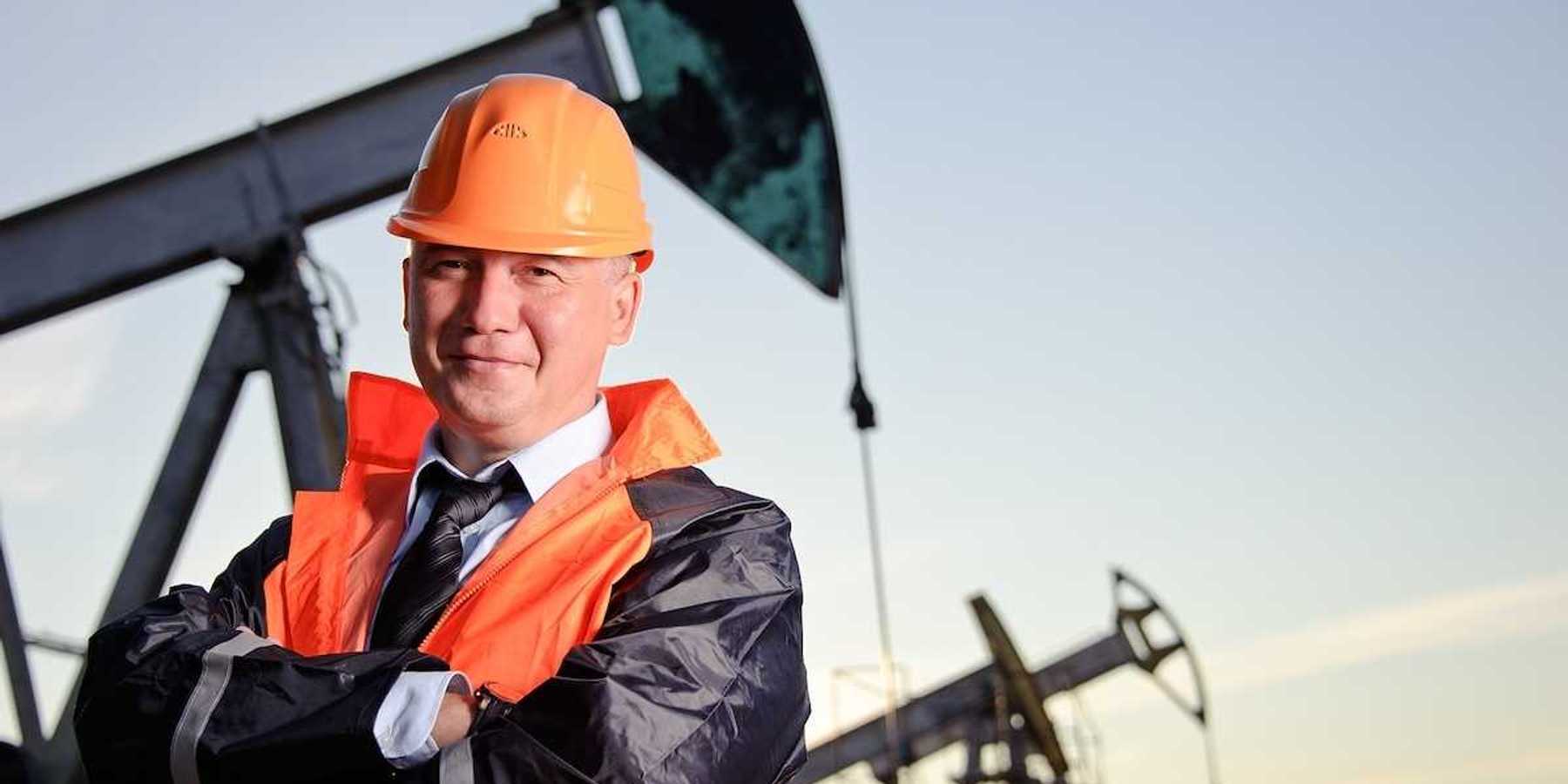 Oil worker in orange uniform and helmet on of background the pump jack and sunset sky.