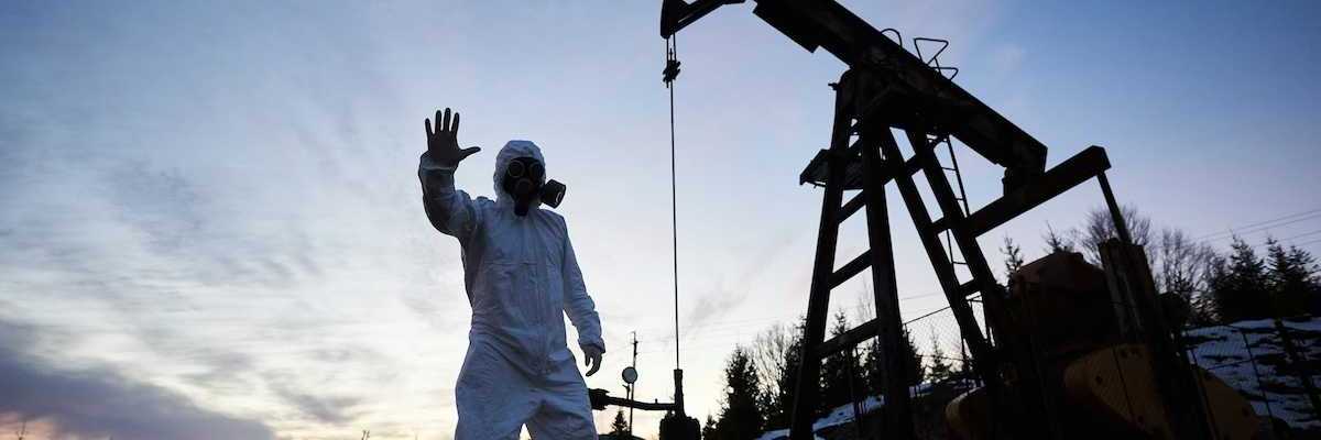 Oilfield drilling site with pump jack and worker wearing a haz-mat suit