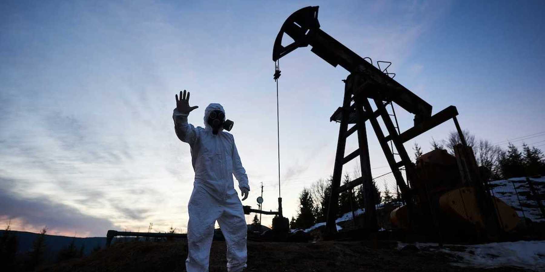 Oilfield drilling site with pump jack and worker wearing a haz-mat suit