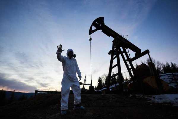 Oilfield drilling site with pump jack and worker wearing a haz-mat suit