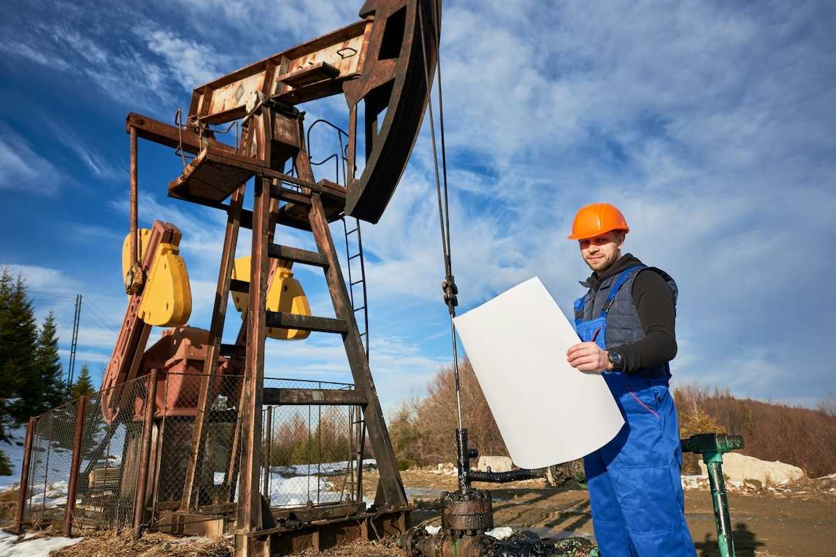 Oilfield worker standing next to a pumpjack and holding a large rectangular piece of paper
