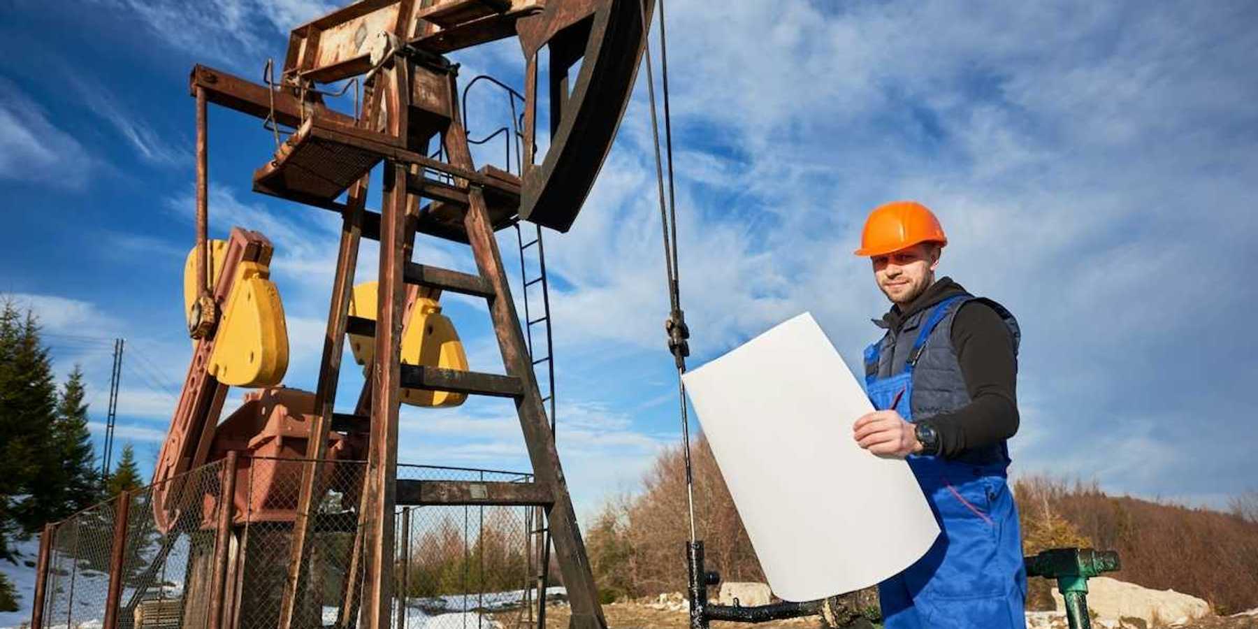 Oilfield worker standing next to a pumpjack and holding a large rectangular piece of paper