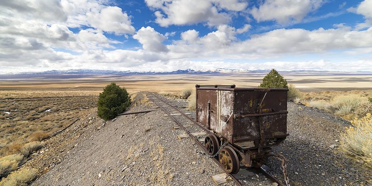 Old mining equipment in the desert with mountains in the background and a cloud-dotted blue sky.