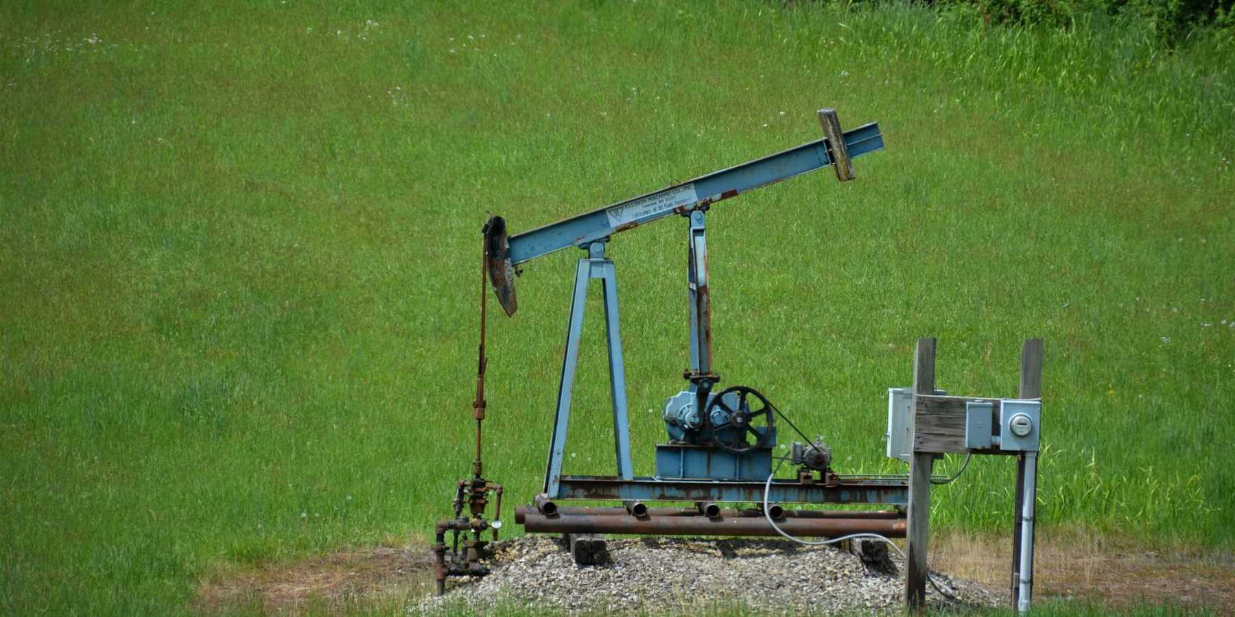 Old oil pump jack in a grassy green field.