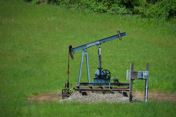 Old oil pump jack in a grassy green field.