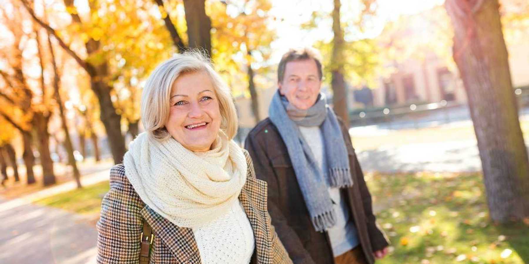 Older couple hand in hand, smiling and strolling on tree-lined walk in Vienna, Austria