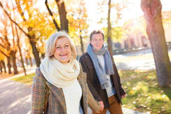Older couple hand in hand, smiling and strolling on tree-lined walk in Vienna, Austria