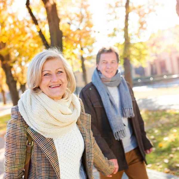 Older couple hand in hand, smiling and strolling on tree-lined walk in Vienna, Austria