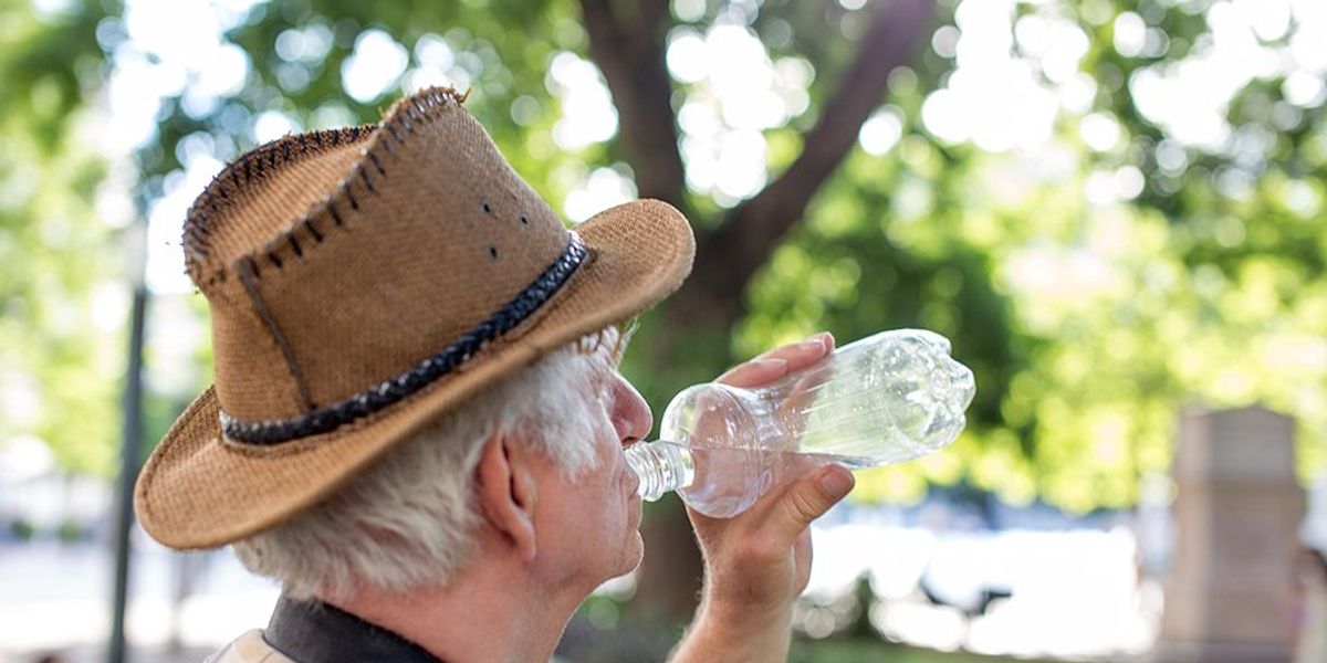 Older man in a straw hat drinking water from a plastic bottle on a hot day.