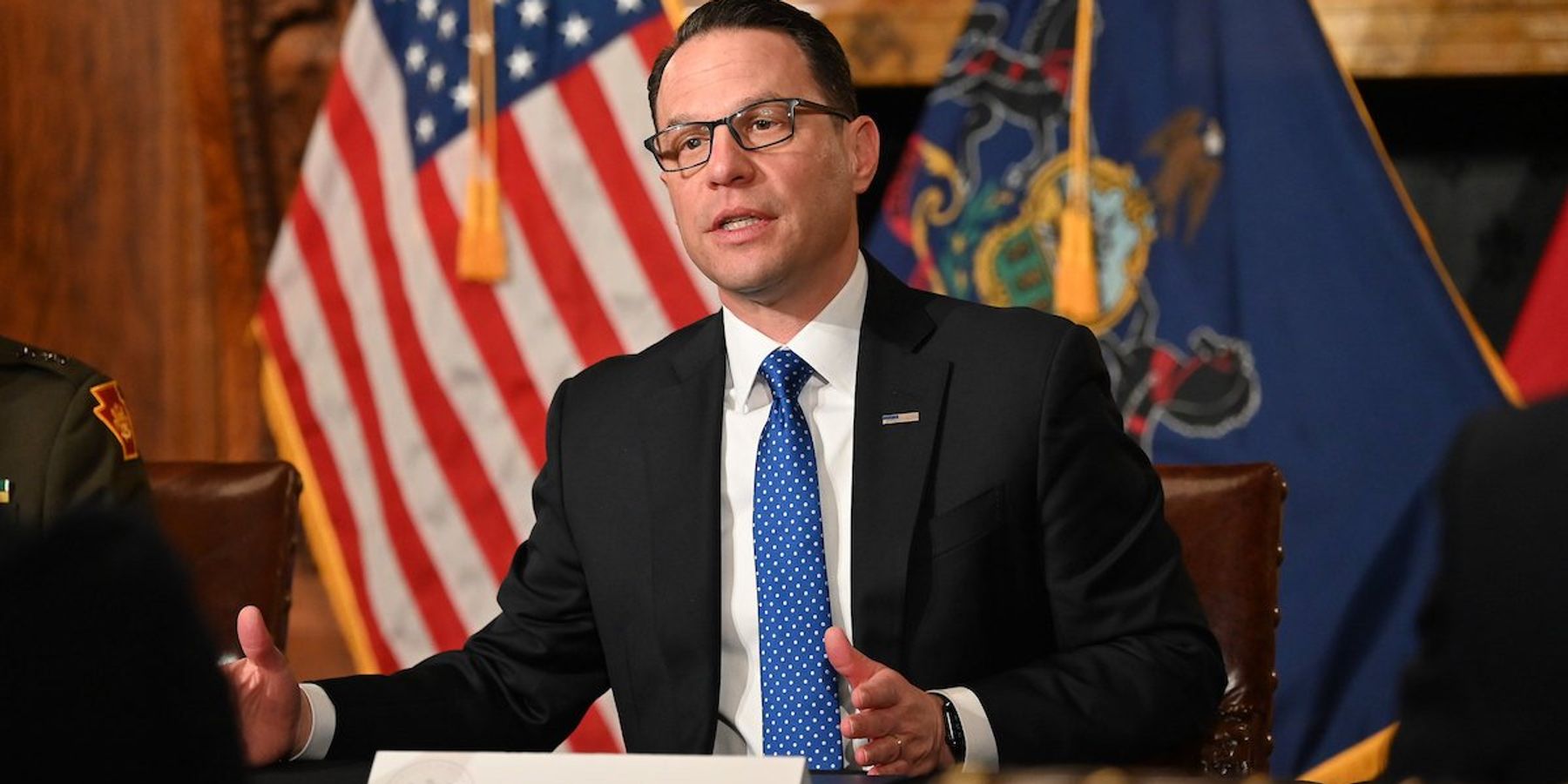 Pennsylvania governor Josh Shapiro speaks with the state flag and American flag behind him.