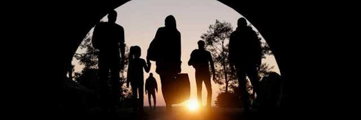 People silhouetted in an arch carrying suitcases and walking toward the setting sun