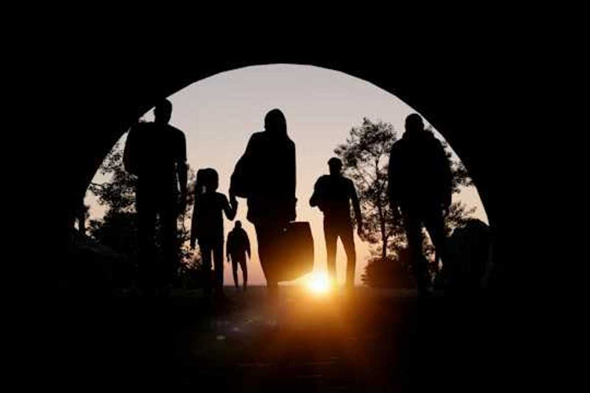 People silhouetted in an arch carrying suitcases and walking toward the setting sun