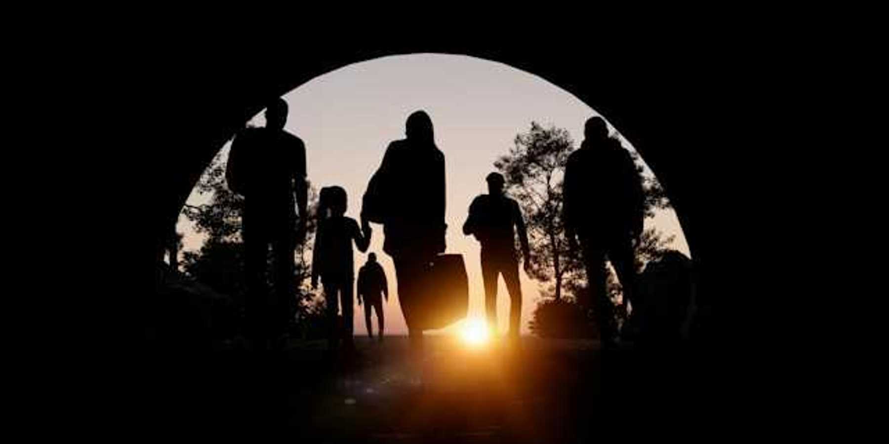 People silhouetted in an arch carrying suitcases and walking toward the setting sun