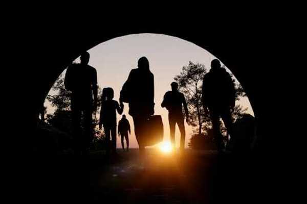 People silhouetted in an arch carrying suitcases and walking toward the setting sun
