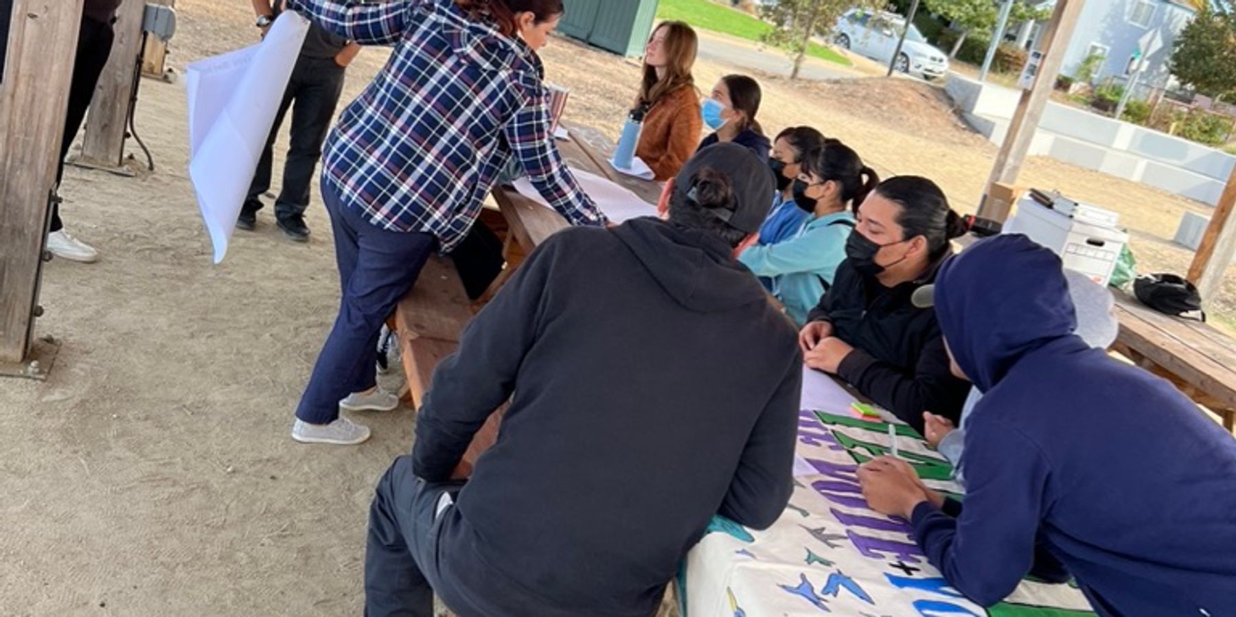 People sitting in an outdoors table working on a big sign.