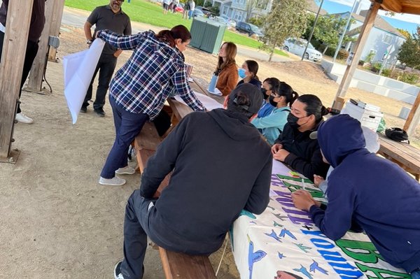 People sitting in an outdoors table working on a big sign.