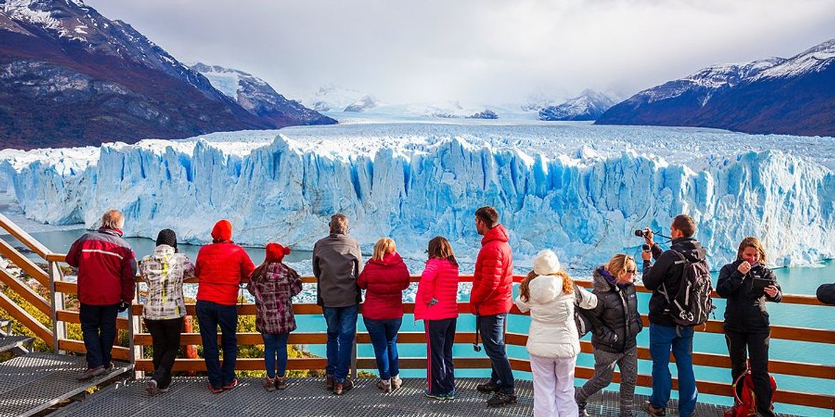 People standing on a viewing platform in front of a glacier.