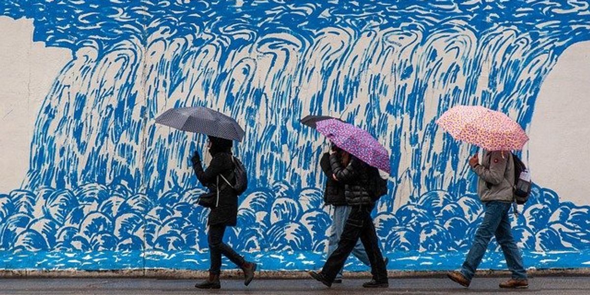 People with umbrellas walking past a wall with a blue mural.