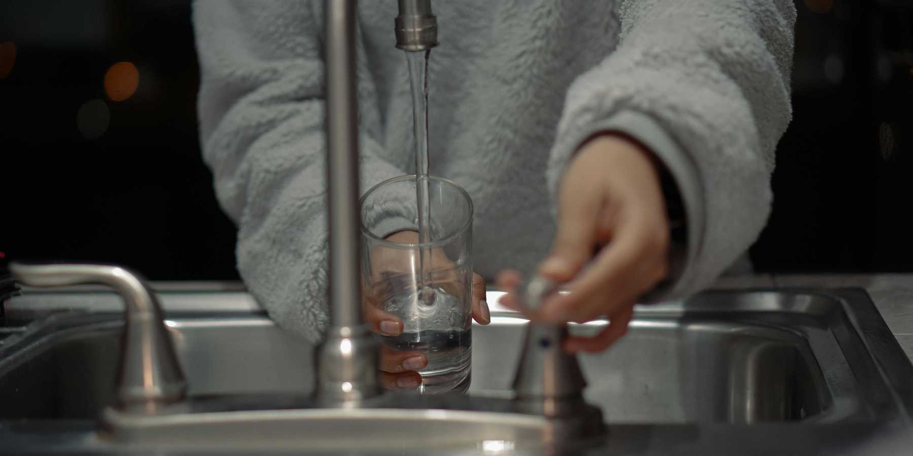 person at sink filling a glass with water.