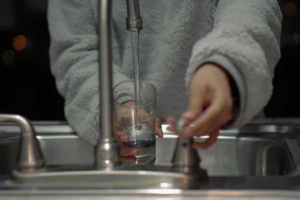 person at sink filling a glass with water.