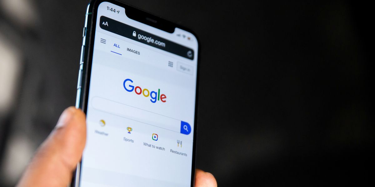 person holding black smartphone with a Google search page on the screen.