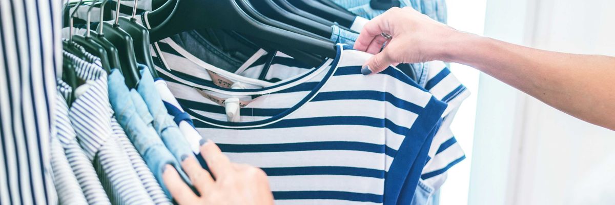 person holding white and black striped shirt on a clothing store rack.