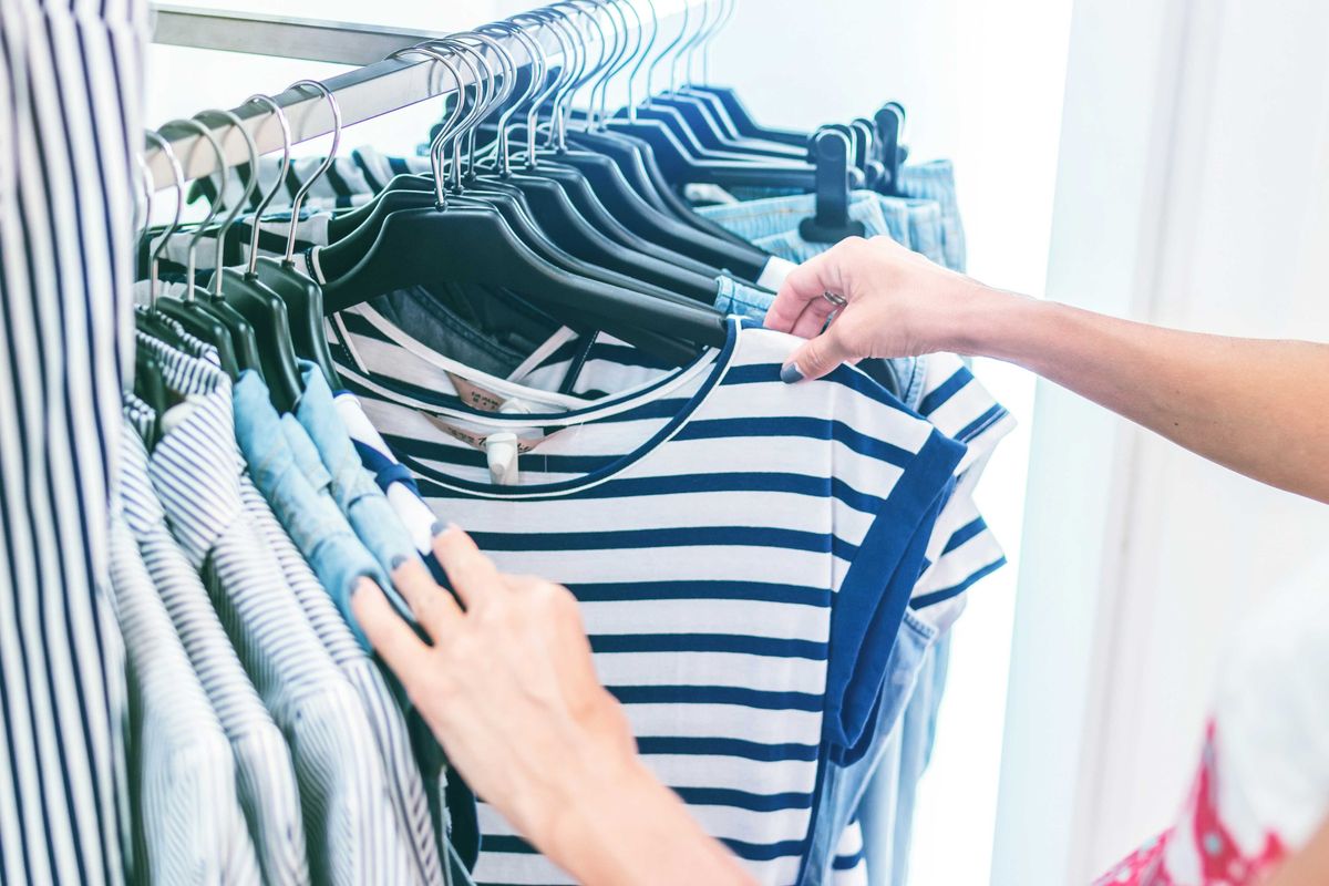 person holding white and black striped shirt on a clothing store rack.