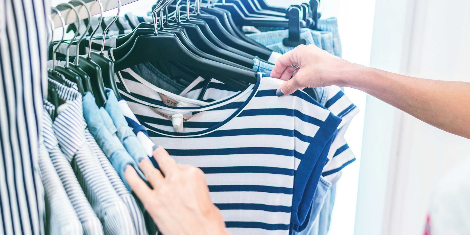 person holding white and black striped shirt on a clothing store rack.