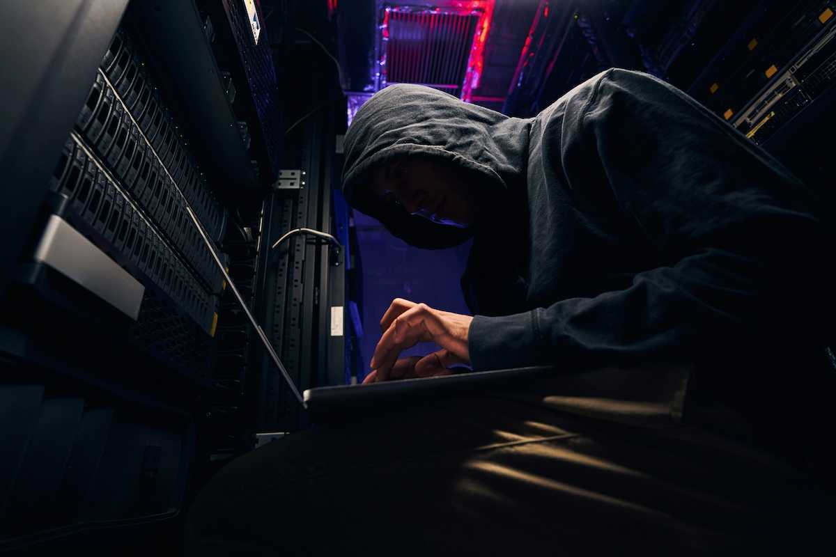 Person in black hoodie, hunched over a keyboard; personification of a shadowy computer hacker