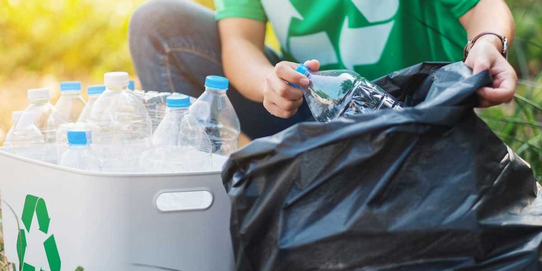 Person in green shirt featuring universal recycling logo sorting plastic boittles from trash bag into recycling container