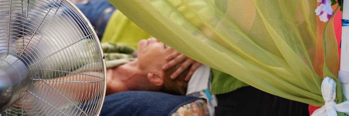 person in supine position receiving massage therapy in front of portable fan