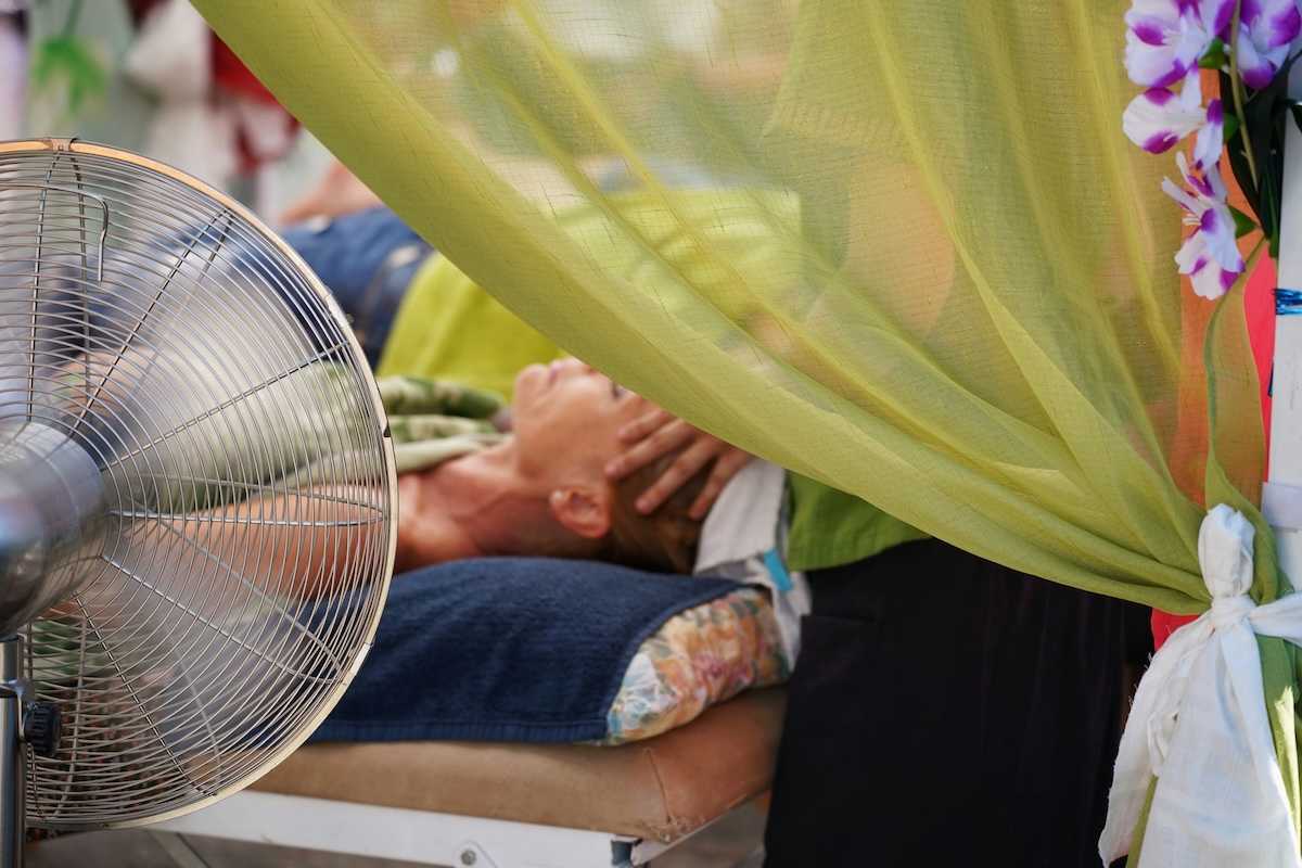 person in supine position receiving massage therapy in front of portable fan