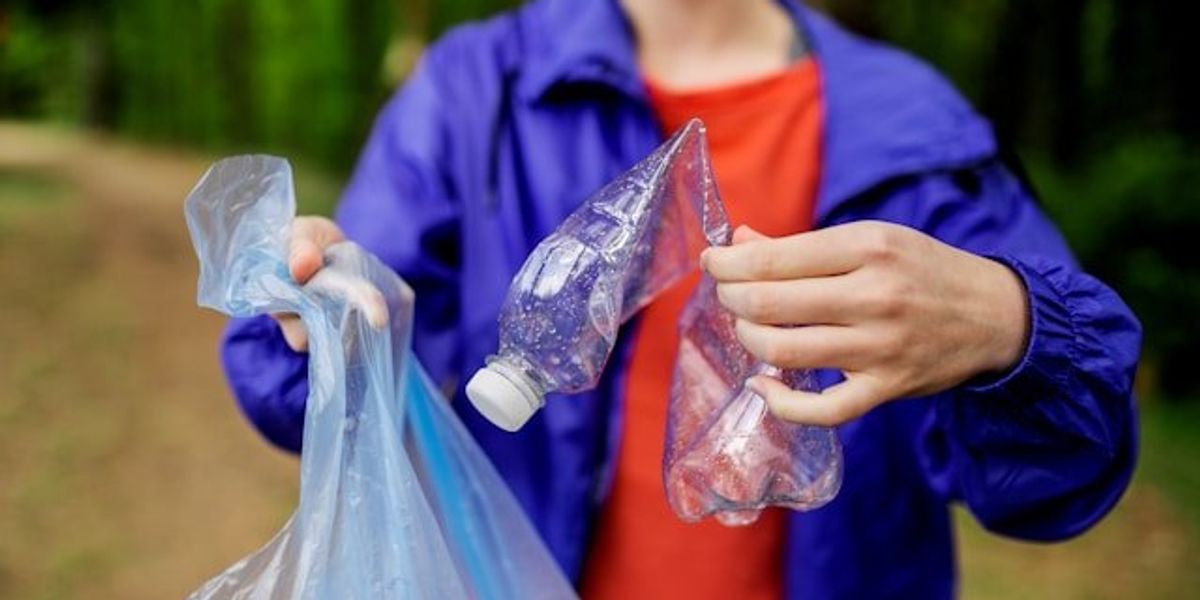 Person placing a plastic bottle into a plastic trash bag.