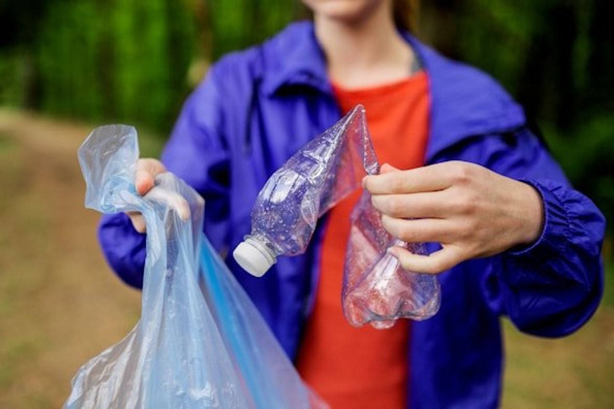 Person placing a plastic bottle into a plastic trash bag.