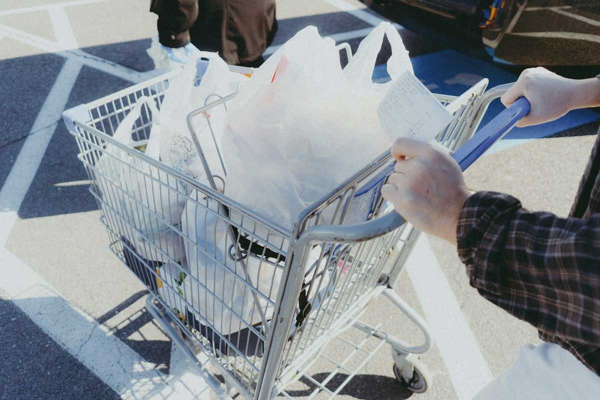 Person pushing a shopping cart filled with shopping items in plastic grocery bags