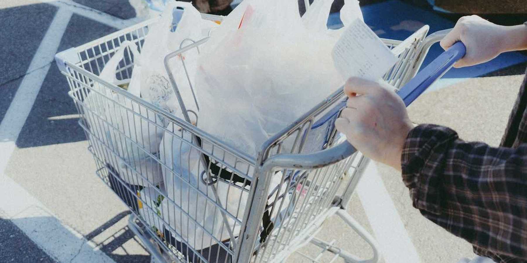 Person pushing a shopping cart filled with shopping items in plastic grocery bags