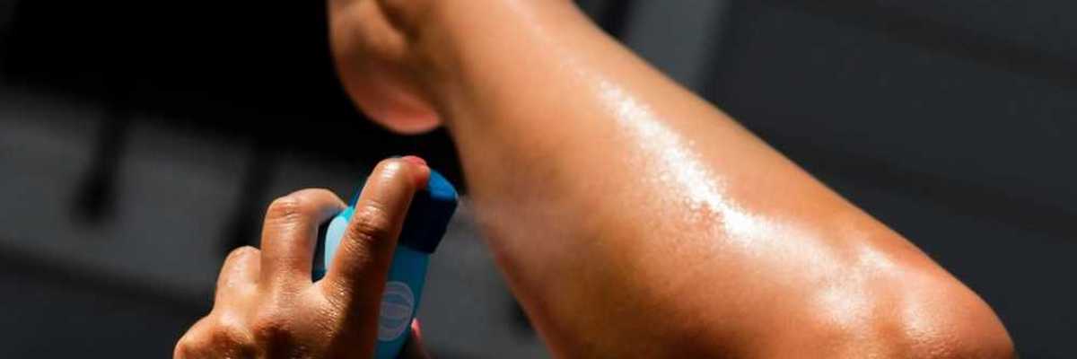 Person spraying sunscreen on left calf using left hand