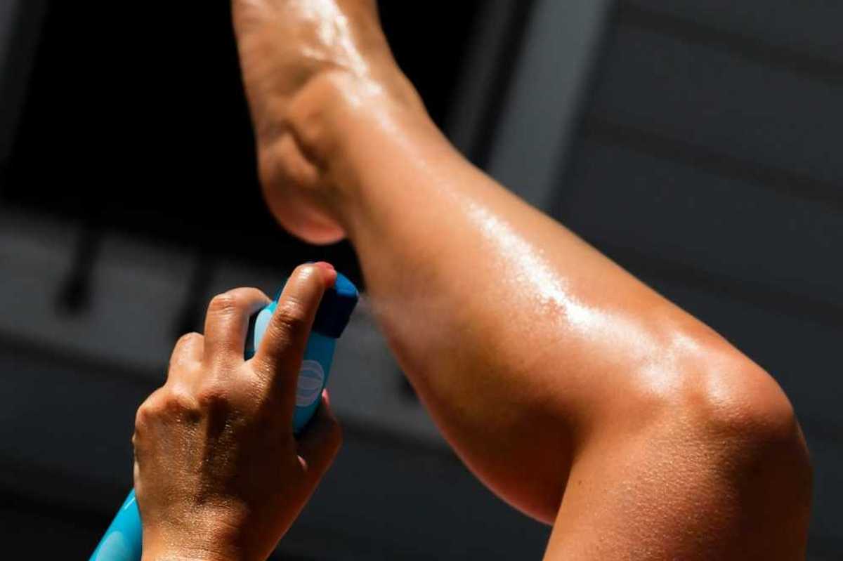 Person spraying sunscreen on left calf using left hand