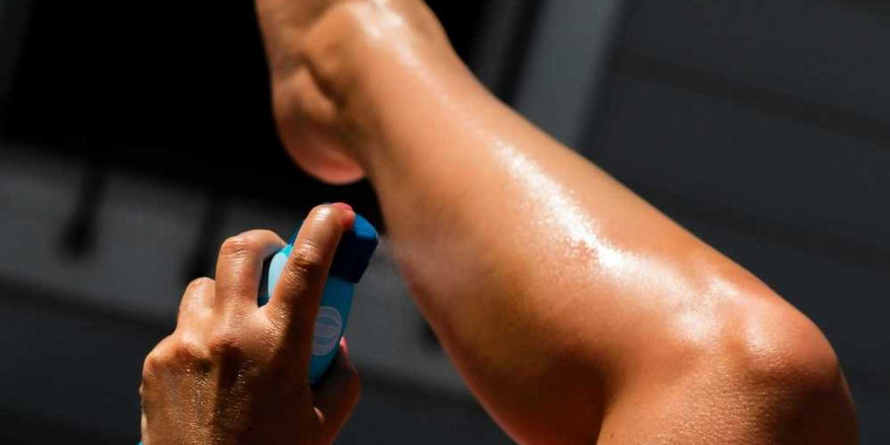 Person spraying sunscreen on left calf using left hand