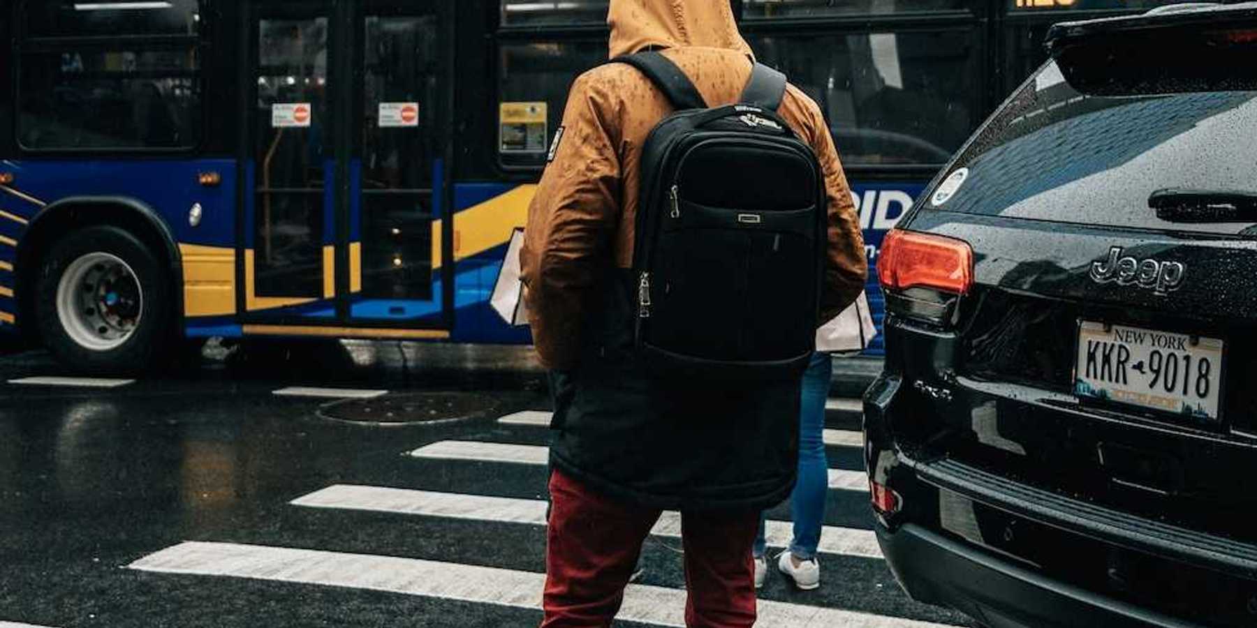 Person standing on curb at crosswalk with a "clean-energy bus" in the background