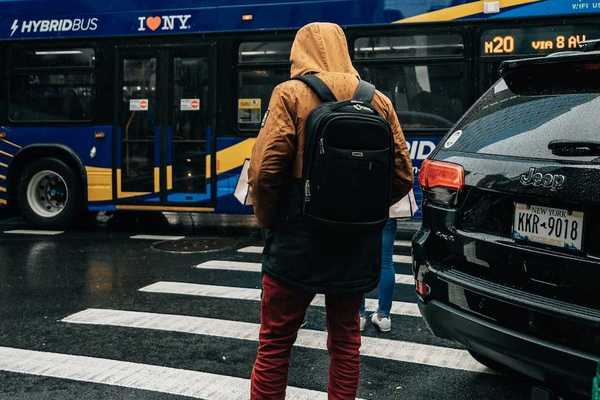 Person standing on curb at crosswalk with a "clean-energy bus" in the background