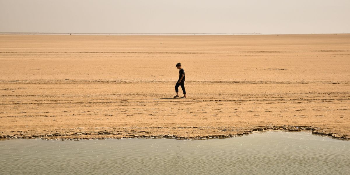 Person walking on dry ground next to small body of water.