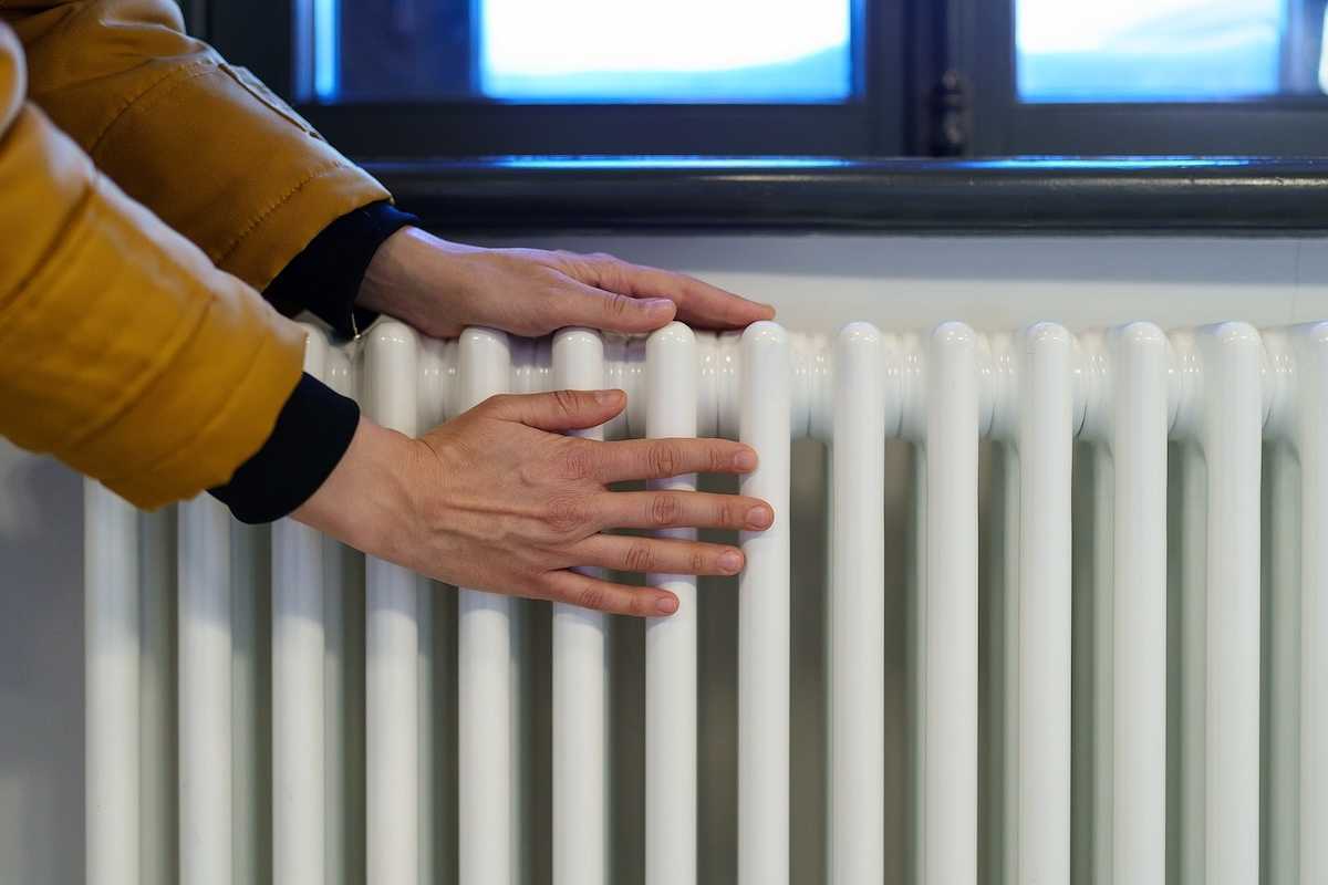 Photo of hands being warmed on an old-fashioned style radiator.