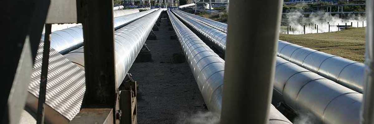 Pipelines extending toward a geothermal energy plant with steam rising from it