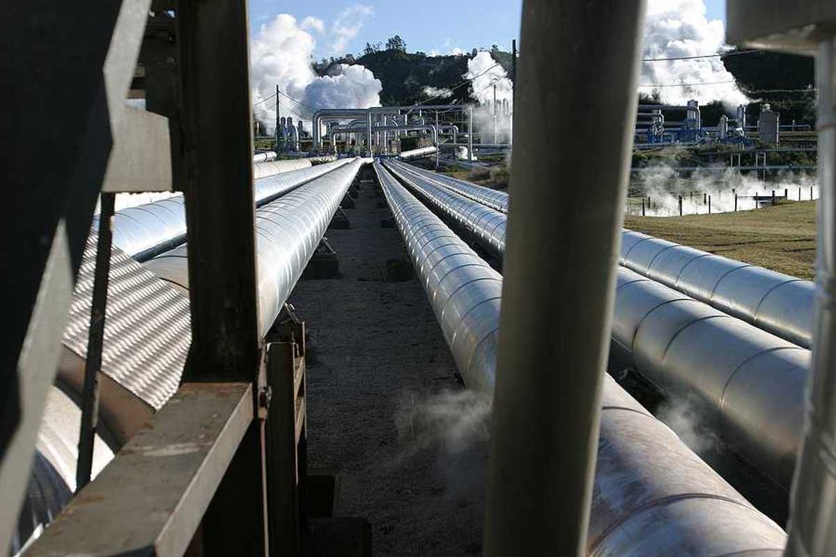 Pipelines extending toward a geothermal energy plant with steam rising from it