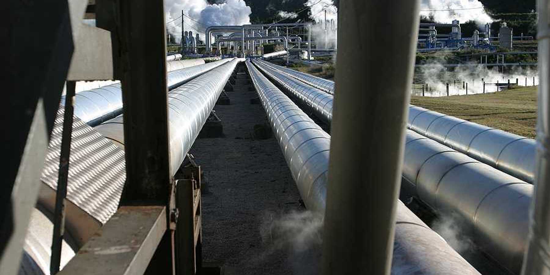 Pipelines extending toward a geothermal energy plant with steam rising from it
